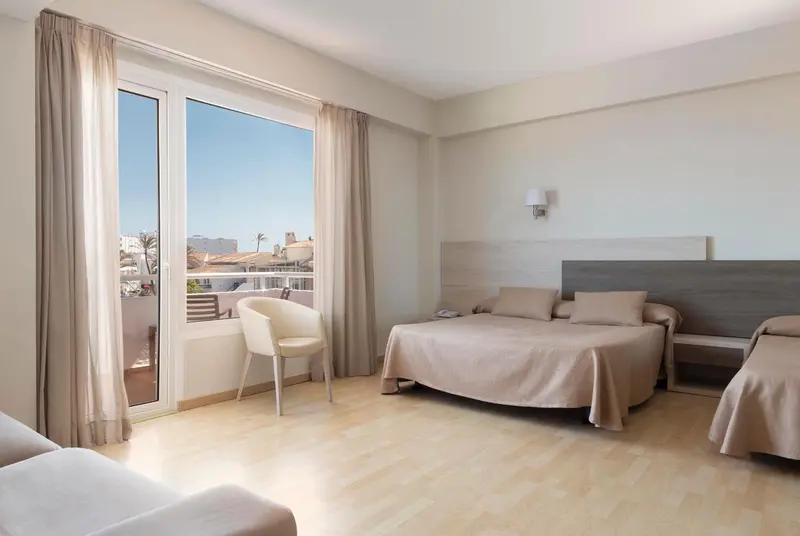Chambre lumineuse avec un lit double et un fauteuil près d'une fenêtre.