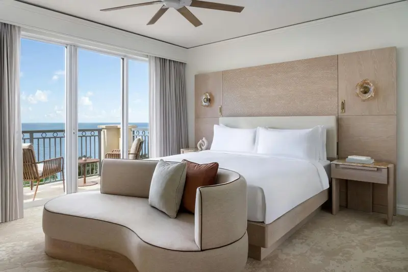 Une chambre lumineuse avec un grand lit et un accès à un balcon avec vue sur la mer.