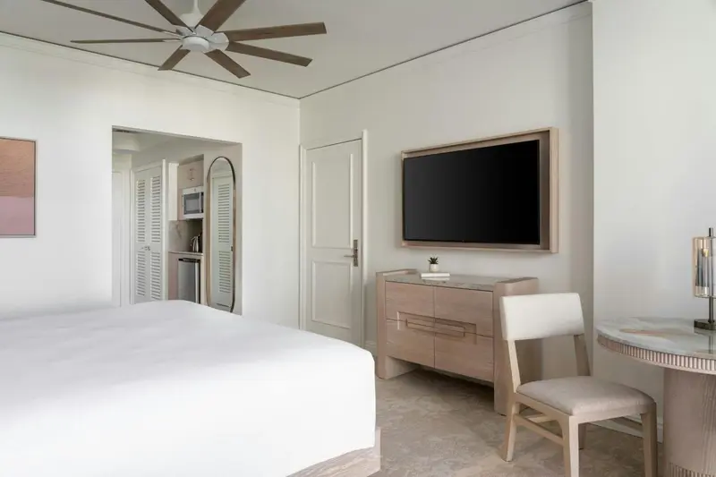 Une chambre lumineuse avec un lit blanc et un téléviseur mural.