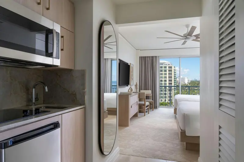 Une kitchenette moderne s'ouvre sur une chambre lumineuse avec vue sur la ville.