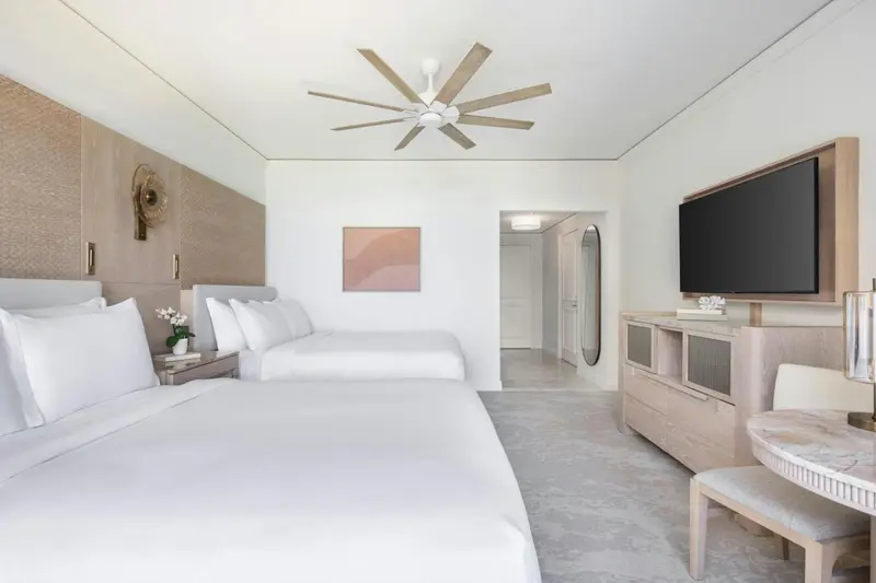 Une chambre lumineuse avec deux lits simples et un téléviseur mural.