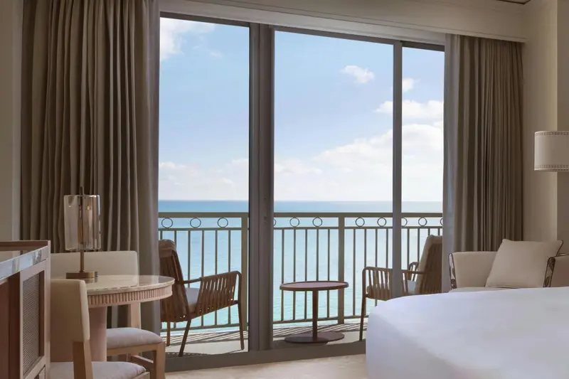 Une chambre lumineuse donne sur une mer turquoise par de grandes baies vitrées.