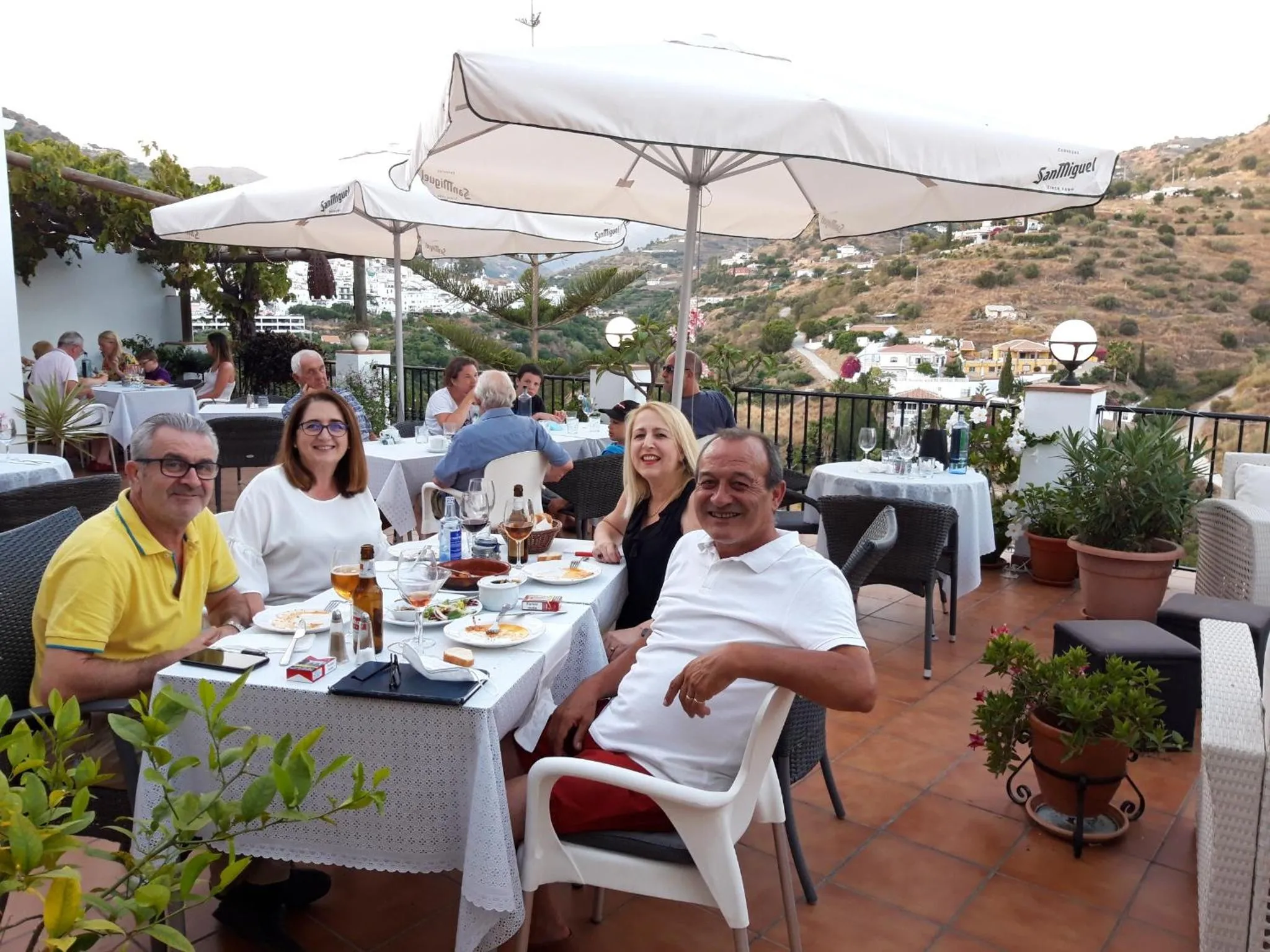 Des convives sont attablés sur une terrasse ensoleillée avec vue sur un paysage montagneux.