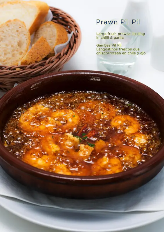 Un plat de crevettes cuites à l'ail et au piment rouge est présenté dans une cocotte en terre cuite.