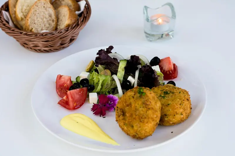 Assiette de salade et de boulettes de légumes avec une sauce jaune et du pain.