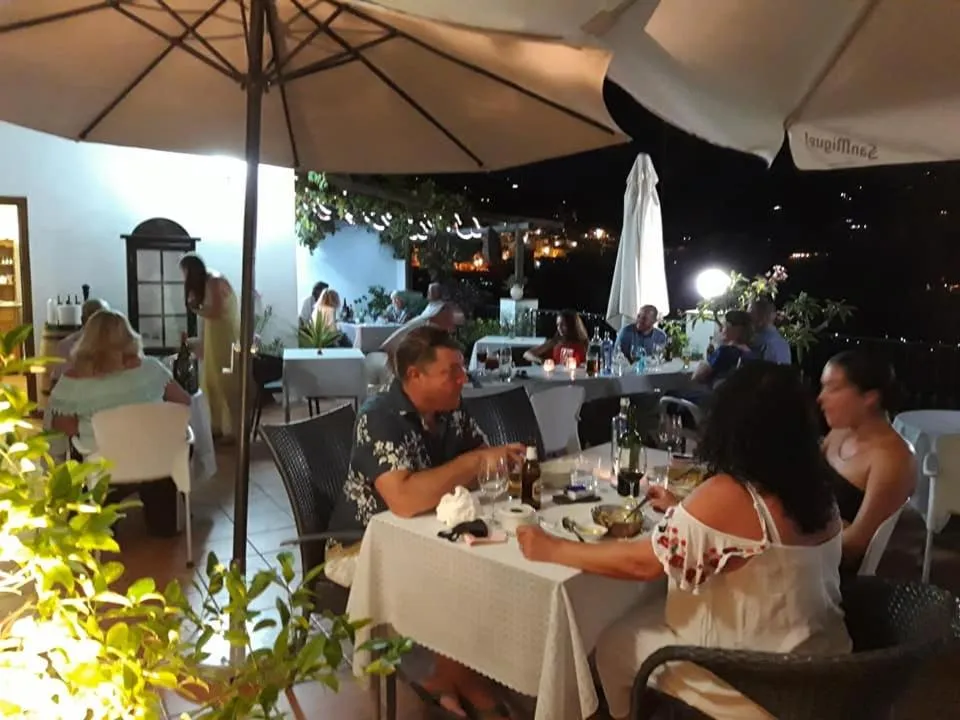 Des convives sont attablés sur une terrasse éclairée le soir.
