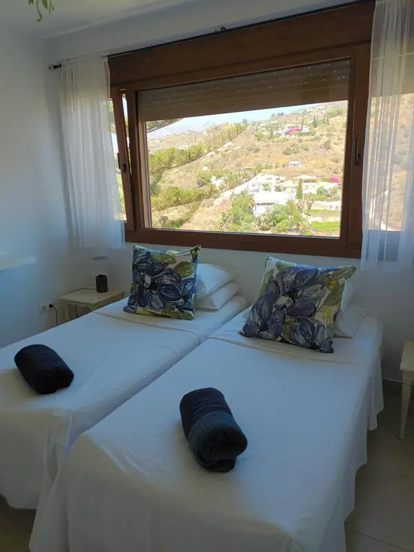 Une chambre lumineuse avec deux lits simples et vue sur une colline.