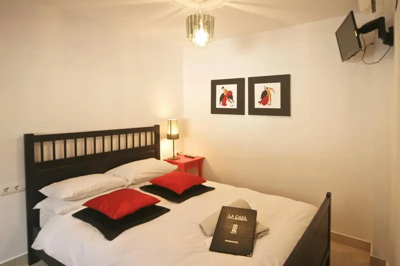 Une chambre lumineuse avec un lit double et des coussins rouges.