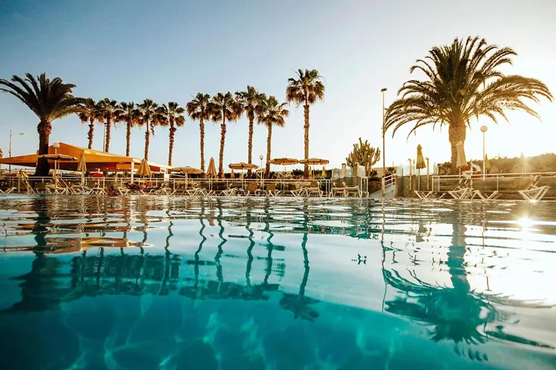 Une piscine turquoise reflète les palmiers et le ciel bleu.