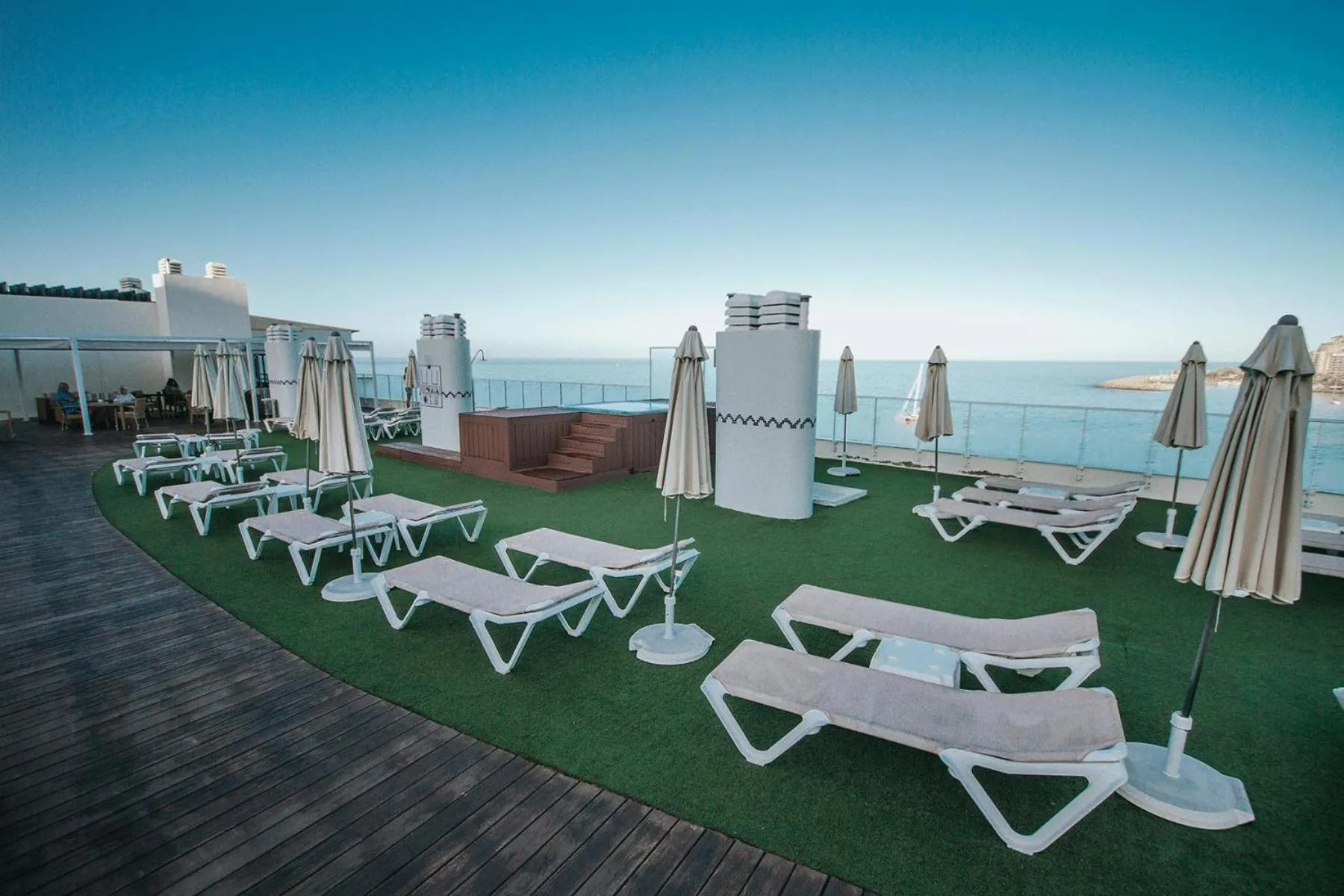 Terrasse aménagée avec transats et gazon synthétique face à la mer.