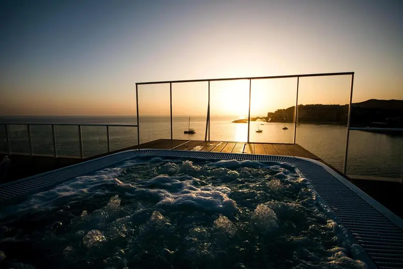 Un jacuzzi sur une terrasse avec vue sur la mer au coucher du soleil.