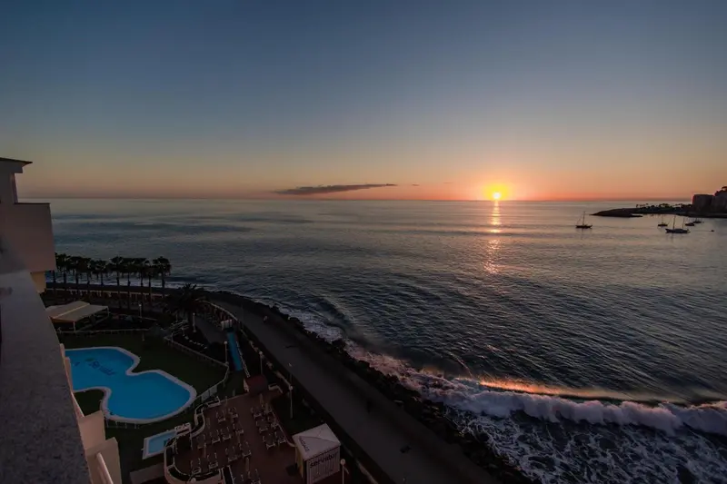 Vue sur la mer au coucher du soleil depuis un balcon avec piscine.