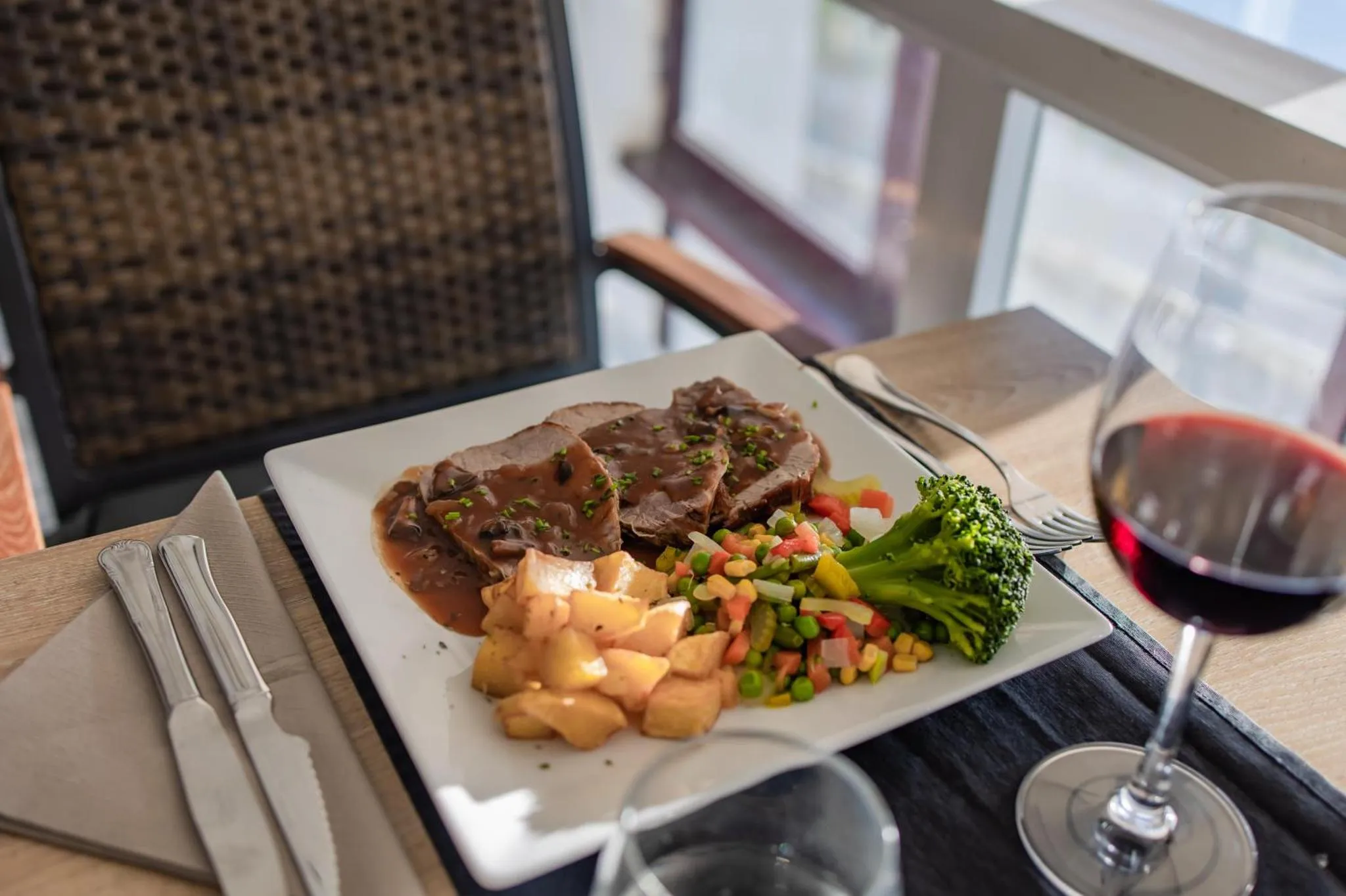 Assiette de viande accompagnée de légumes et de vin sur une table.