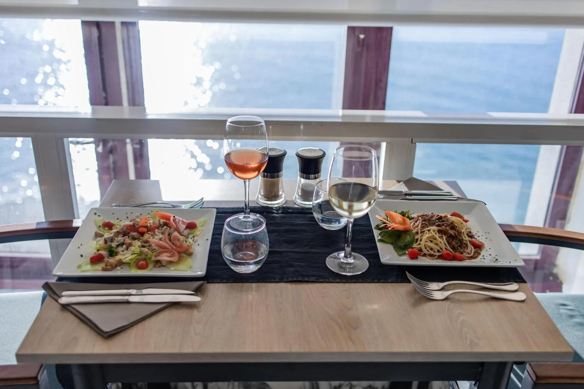 Une table est dressée avec des plats et des boissons face à une vue sur la mer.