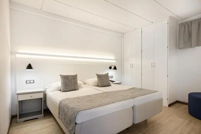 Une chambre lumineuse avec deux lits simples et des meubles blancs.