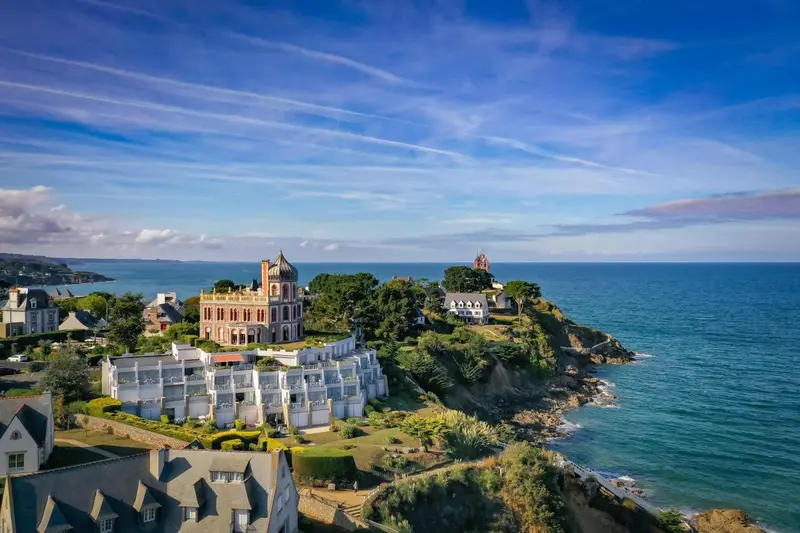 Vue aérienne d'un bâtiment blanc et rose sur une côte rocheuse.