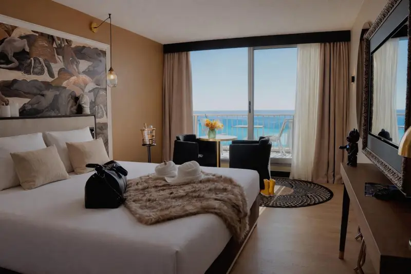Une chambre lumineuse avec un grand lit et un balcon offrant une vue sur la mer.