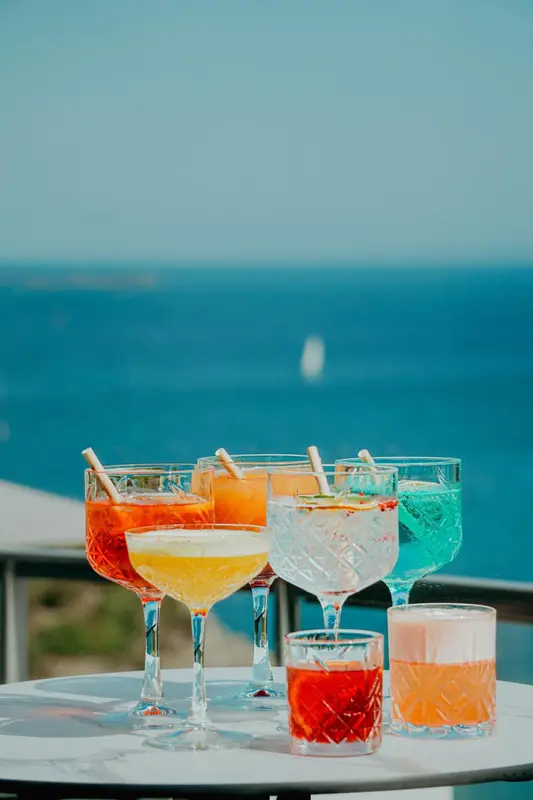 Des cocktails colorés sont présentés sur une table en verre avec vue sur la mer.