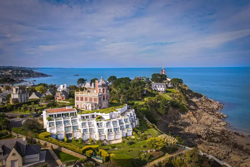 Vue aérienne d'un bâtiment blanc et d'une côte rocheuse avec une mer bleue.