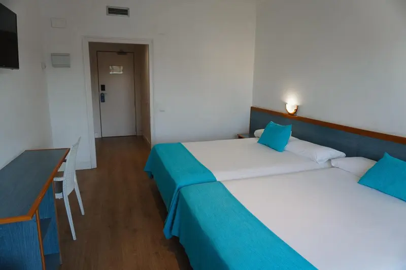 Une chambre lumineuse avec un lit turquoise et un bureau.