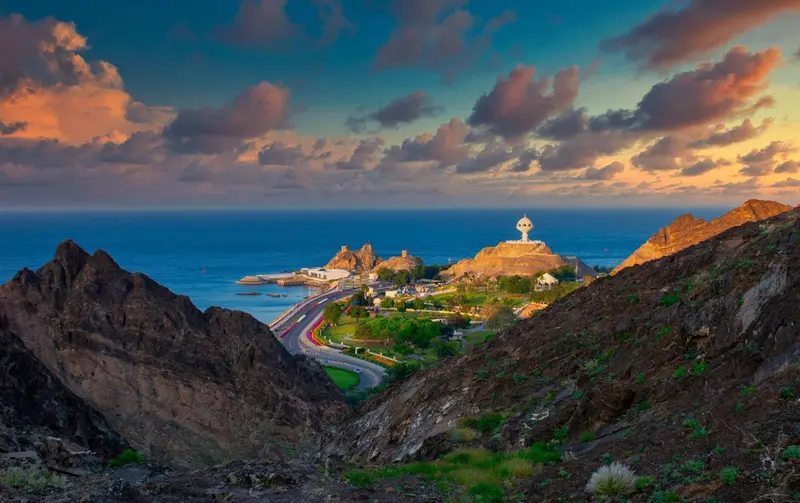 Vue panoramique sur une côte rocheuse et une ville côtière au coucher du soleil.