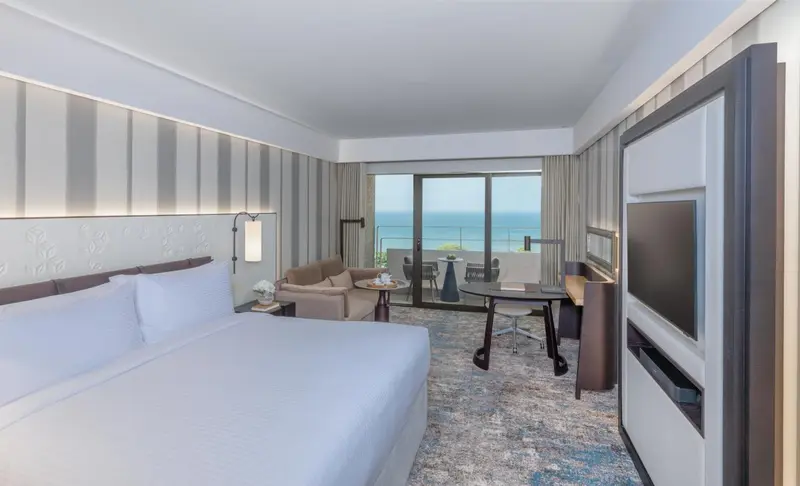 Chambre lumineuse avec un grand lit et une vue sur la mer par une baie vitrée.