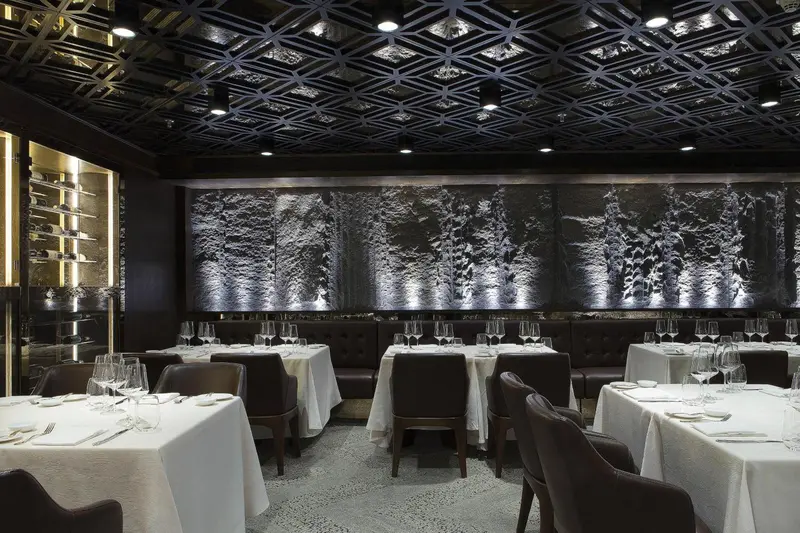 Une salle de restaurant élégante avec des tables dressées et un décor mural artistique.