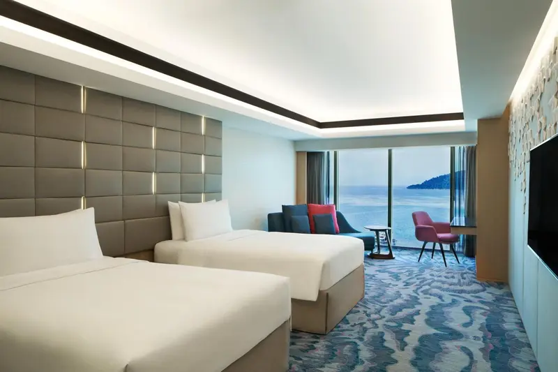 Chambre lumineuse avec deux lits et vue sur la mer.