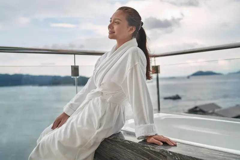 Une femme en peignoir contemple la mer depuis une terrasse.