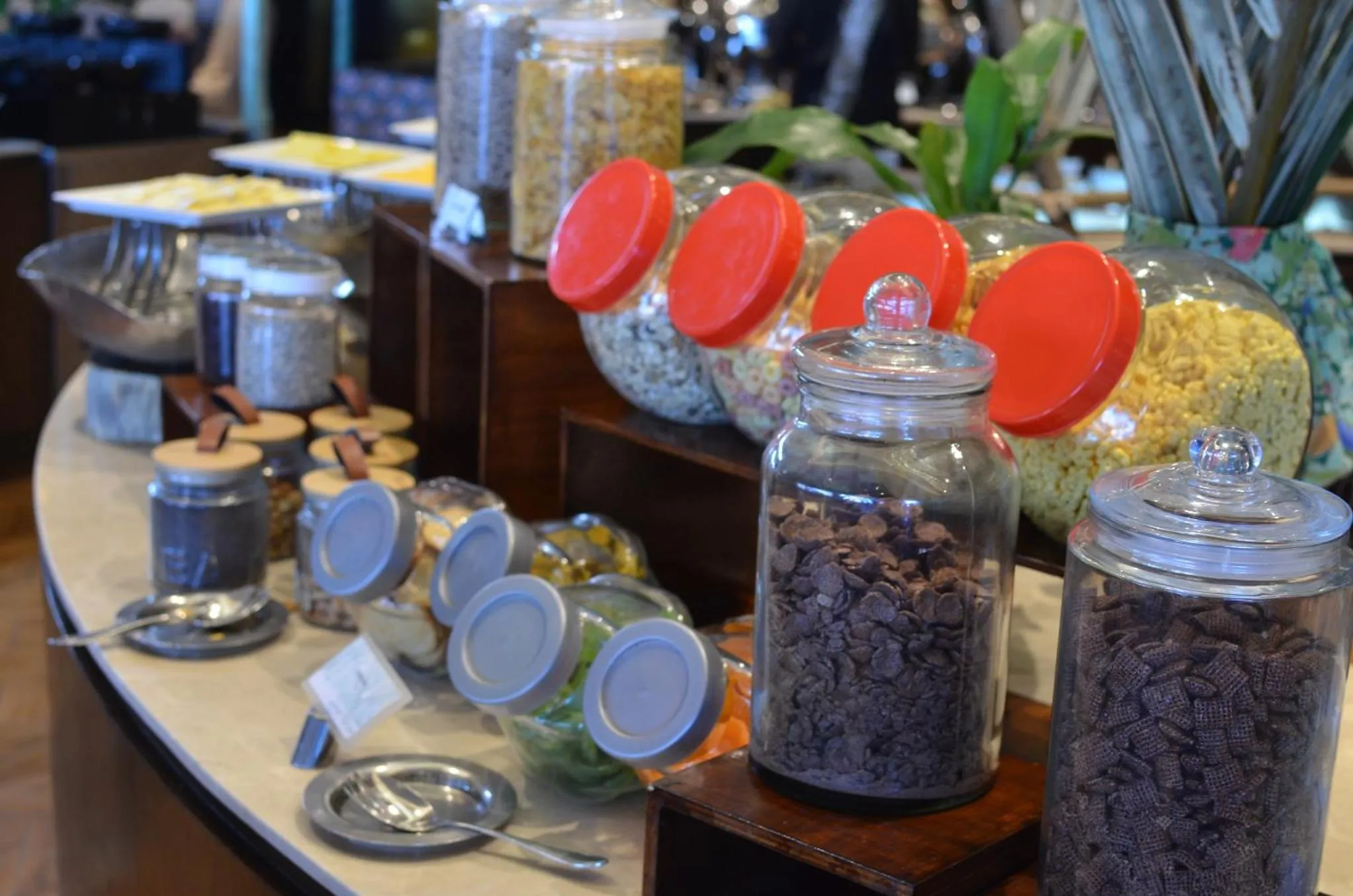 Un buffet propose une variété de céréales et de fruits secs dans des bocaux en verre.