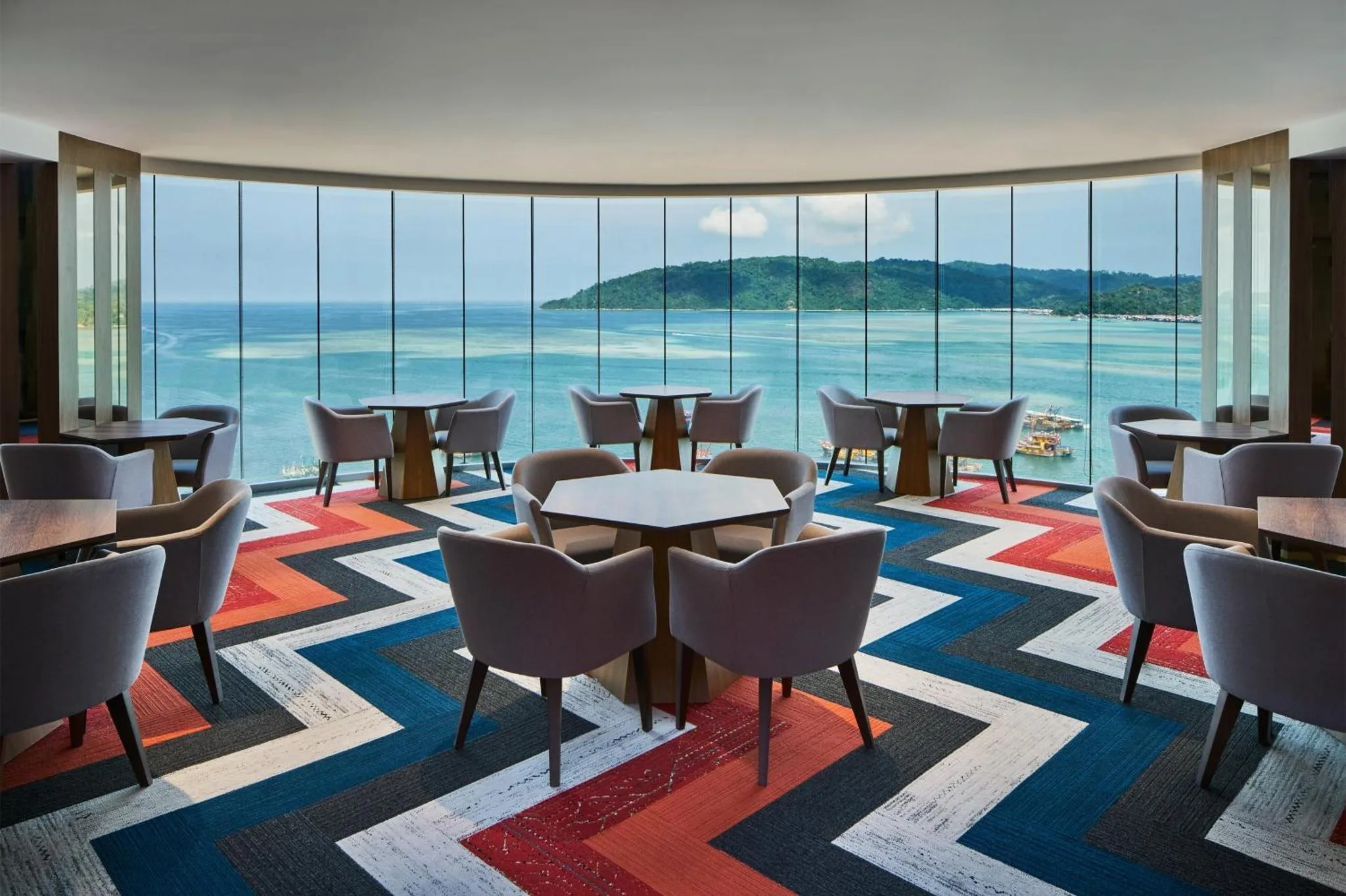 Un espace de détente avec des tables et des fauteuils face à une grande baie vitrée donnant sur la mer.