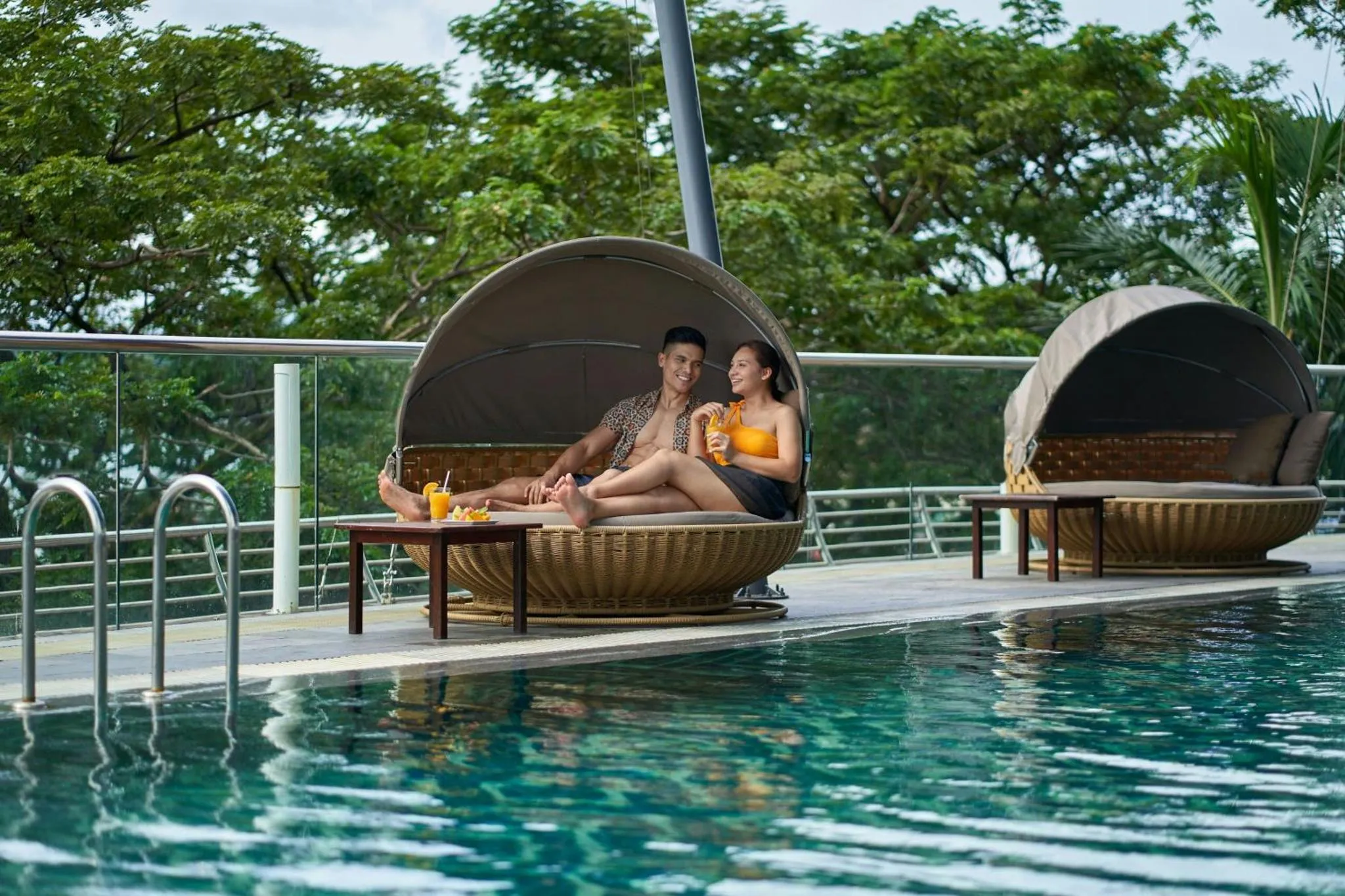 Un couple se détend dans des fauteuils suspendus au bord d'une piscine.