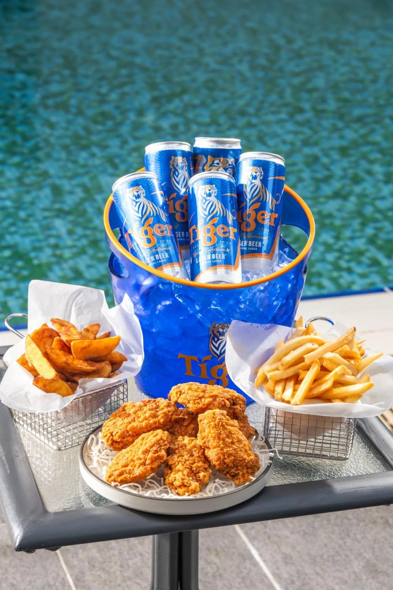 Une table propose des boissons fraiches et des accompagnements croustillants au bord d'une piscine.
