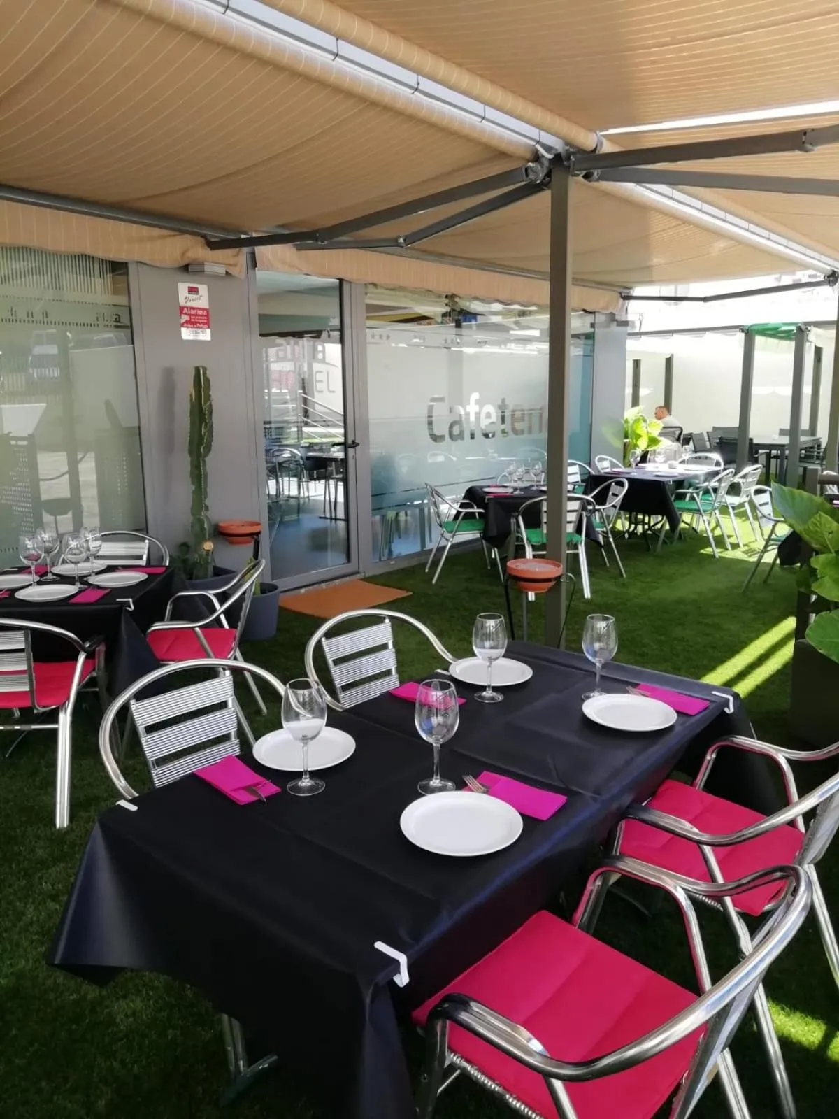 Tables dressées sur une terrasse ombragée avec des chaises roses et des nappes noires.