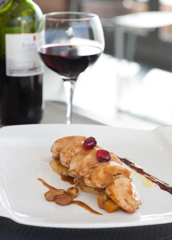 Assiette de volaille nappée de sauce, accompagnée d'une garniture et d'une coupe de vin rouge.