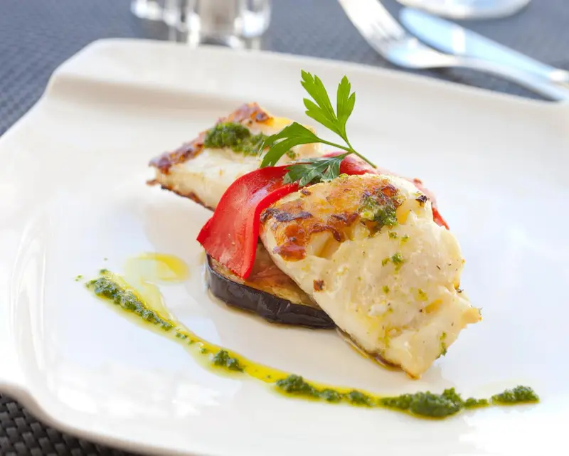 Assiette de poisson grillé avec légumes et sauce verte.