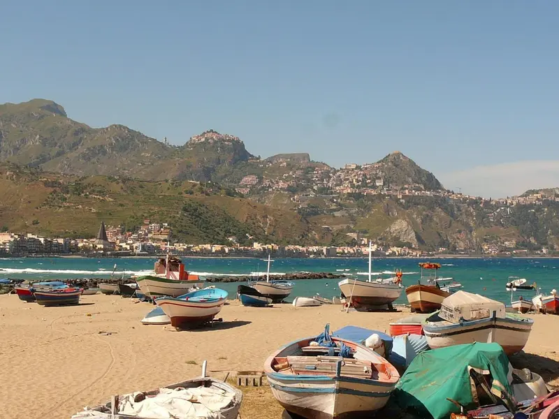 Des bateaux de pêche colorés échoués sur une plage de sable fin, avec une côte montagneuse en arrière-plan.