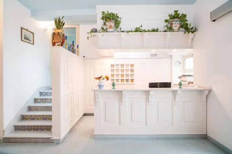 Un comptoir d'accueil blanc se trouve devant un escalier décoré de céramiques colorées.