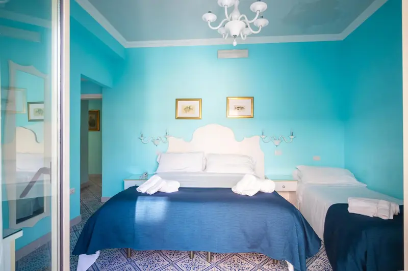 Chambre lumineuse avec un lit recouvert d'une courtepointe bleue et de coussins blancs.