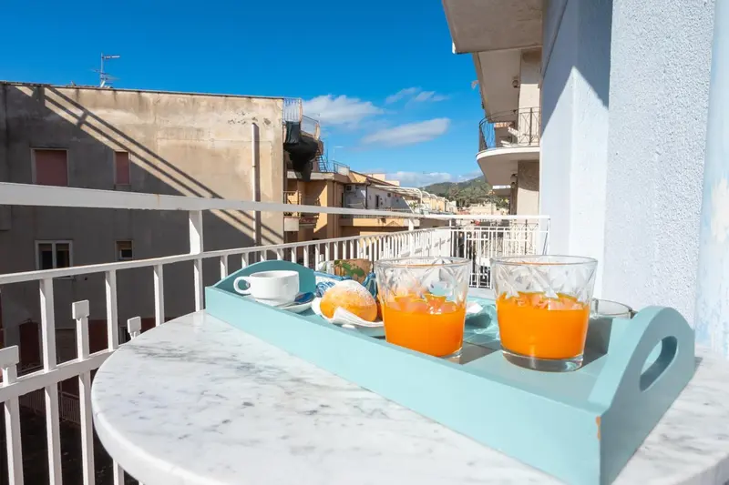 Une table ronde en marbre présente un petit-déjeuner avec des jus d'orange et des fruits sur une terrasse ensoleillée.