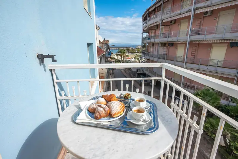 Une table ronde avec un petit-déjeuner est posée sur un balcon avec vue sur la ville et la mer.