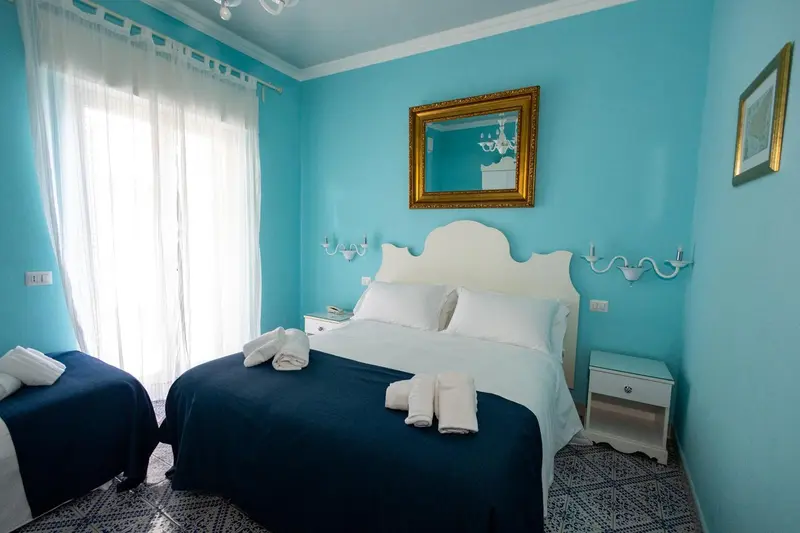 Une chambre lumineuse avec un lit blanc et des murs turquoise.