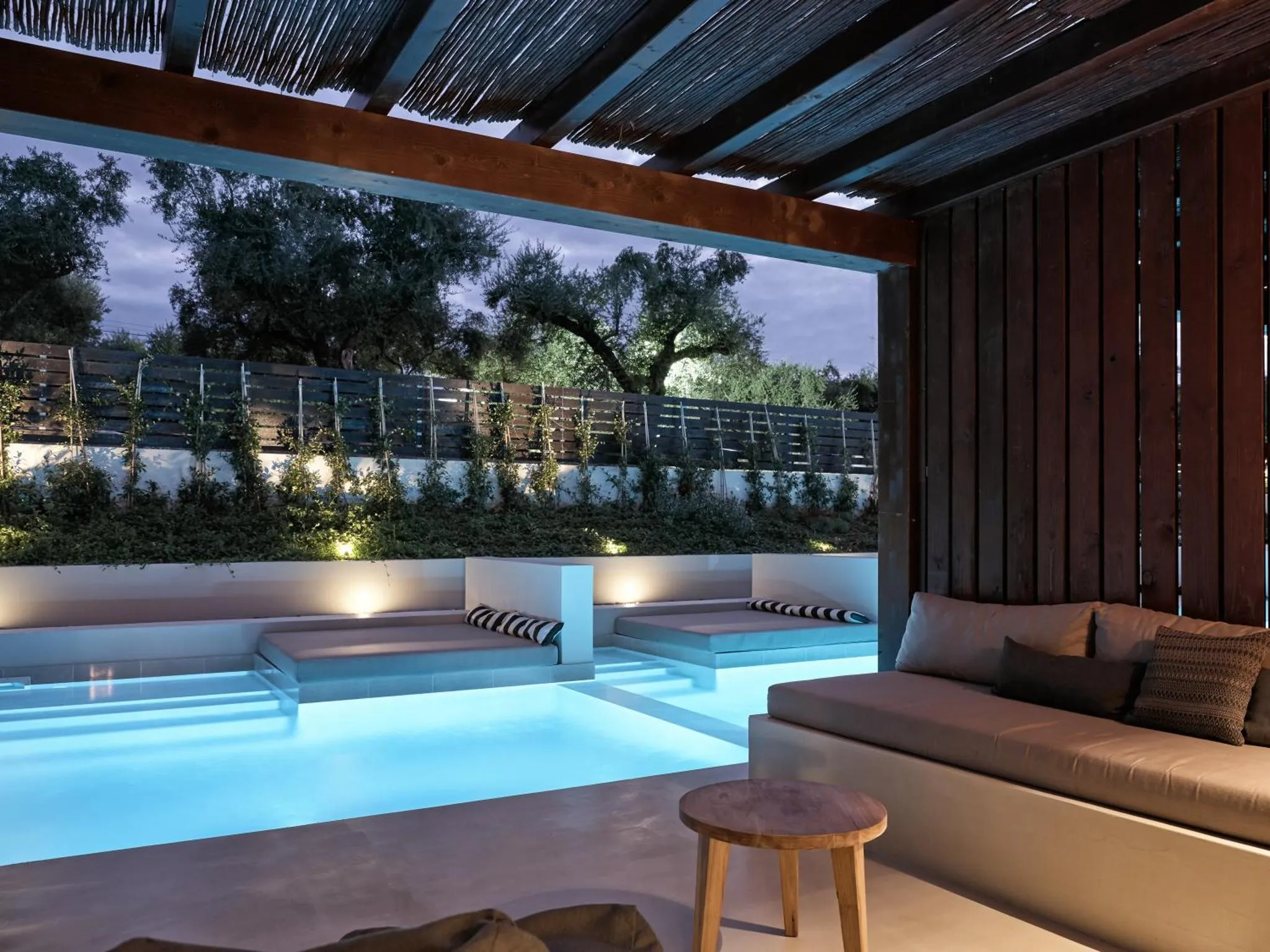 Une piscine éclairée avec des transats et un espace détente ombragé.