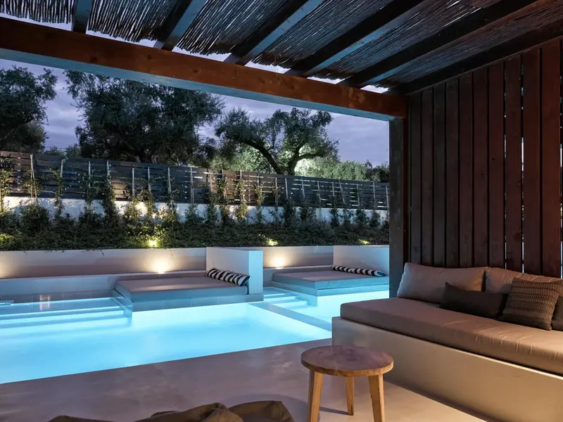 Une piscine éclairée avec des transats et un espace détente ombragé.