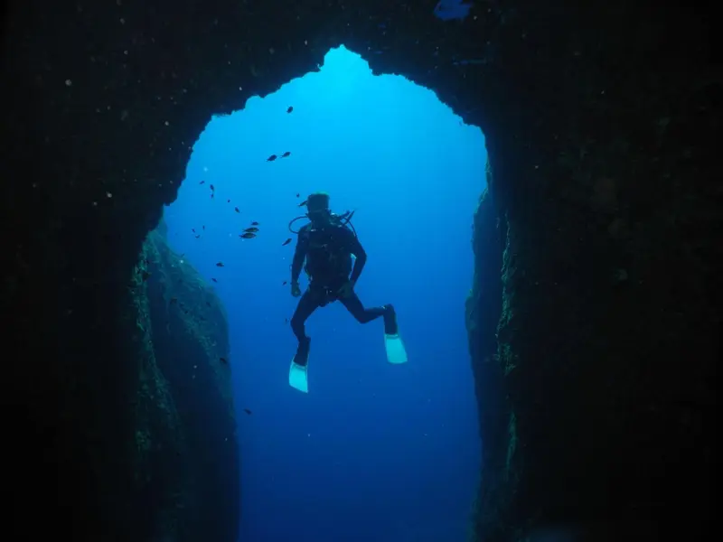 Un plongeur explore une arche rocheuse sous-marine.