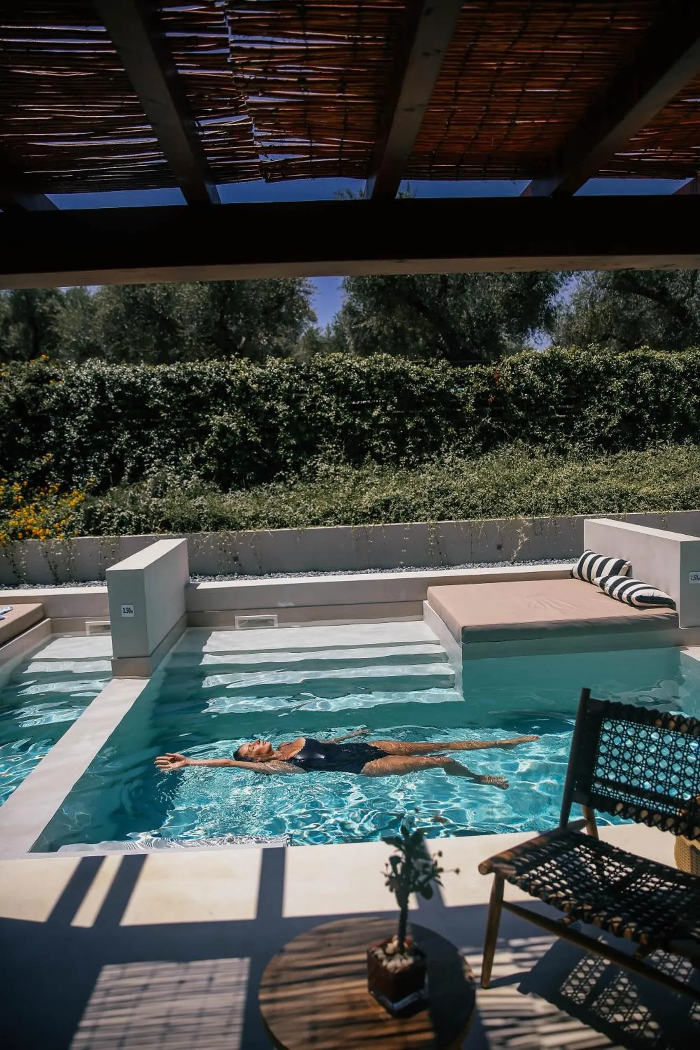 Une personne se détend dans une piscine rectangulaire entourée d'une terrasse ombragée.