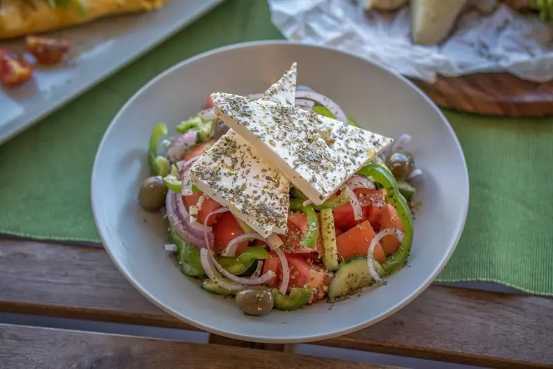 Une salade grecque avec du fromage feta, des tomates, des concombres et des olives est présentée sur une table.