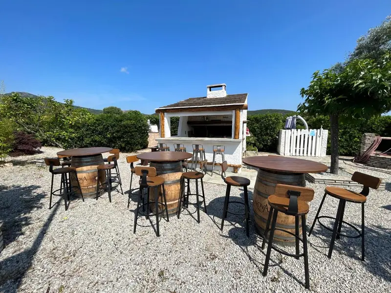 Terrasse ombragée avec tables et chaises en bois autour d'un bar extérieur.
