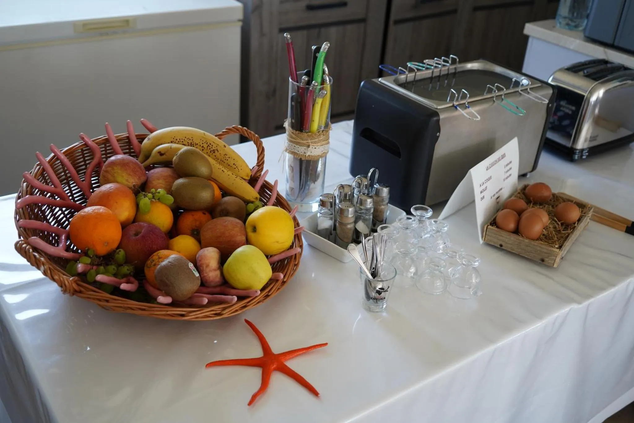 Une table blanche présente un panier de fruits frais et des œufs.