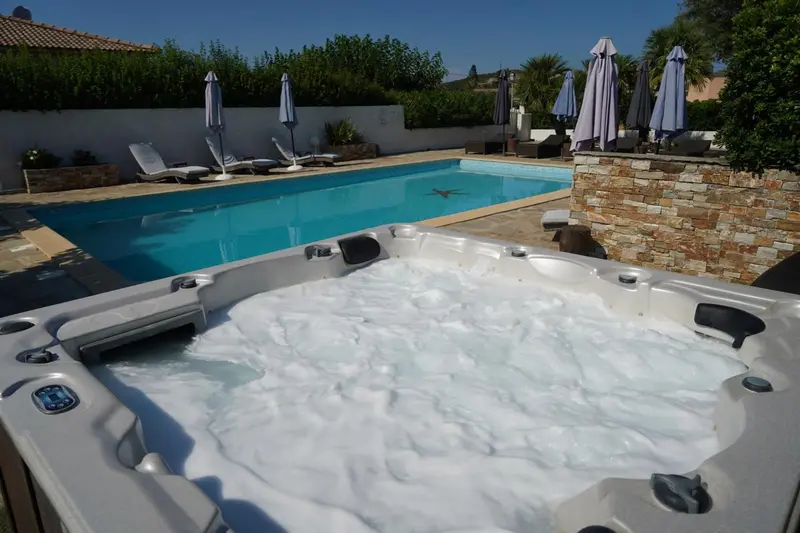 Jacuzzi et piscine ensoleillés avec transats et parasols.